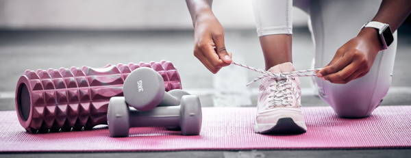 Gewichte und eine Frau, die ihre Schuhe vor dem Training im Fitnessstudio bindet